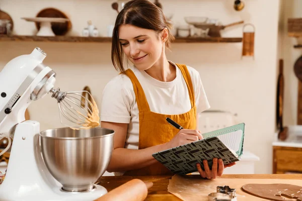 Sorridente Pasticciera Donna Annotando Note Mentre Biscotti Natale Cucina Accogliente — Foto Stock