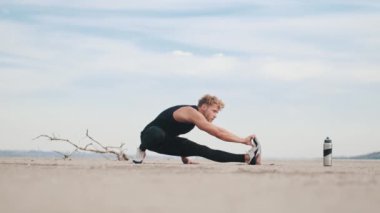 A focused young sportsman is doing stretching exercises on his legs while training outdoors