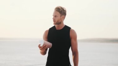 A handsome young sportsman is shaking his bottle while training outdoors