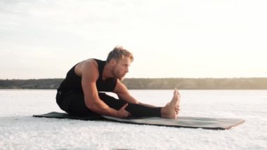 A concentrated young athlete is doing yoga outside on the yoga mat