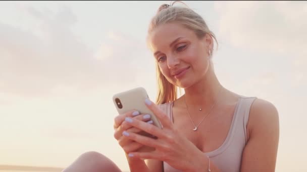 Pleased Young Blonde Woman Using Her Smartphone Sitting Yoga Mat — Vídeo de Stock