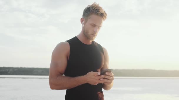 Handsome Young Athlete Using His Smartphone Standing — Stockvideo