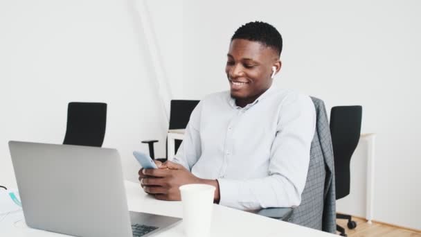 Pleased Black Guy Earbuds Using His Smartphone While Working Office — Wideo stockowe