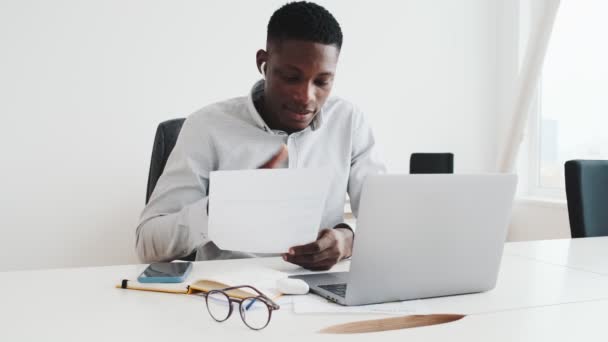 一个戴耳塞的英俊黑人坐在办公室里用这台笔记本电脑和视频连接聊天 — 图库视频影像