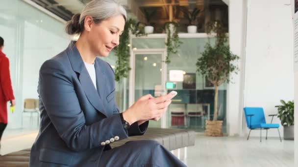 Pleased Elder Businesswoman Using Her Smartphone While Sitting Conference Room — Stock videók