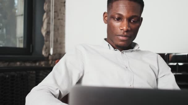 Hombre Afroamericano Positivo Está Usando Computadora Portátil Sentada Silla Dentro — Vídeo de stock