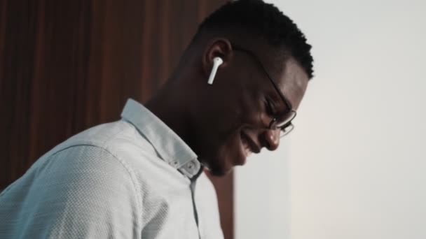 一位戴着无线耳机的快乐的非洲商人走进了阁楼公寓 — 图库视频影像