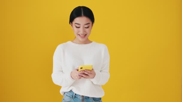 아시아인 스마트폰을 사용하여 스튜디오의 노란색 고립된 카메라에 미소를 — 비디오