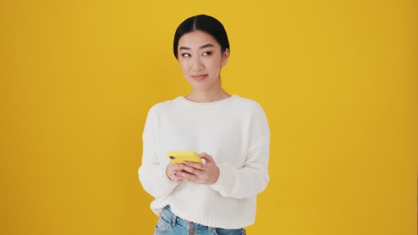 Tänkande Asiatisk Kvinna Använder Sin Smartphone Stående Isolerad Över Gul — Stockvideo