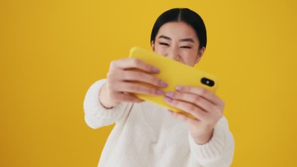 Egy Boldog Ázsiai Játszik Smartphone Áll Elszigetelt Sárga Fal Stúdióban — Stock videók