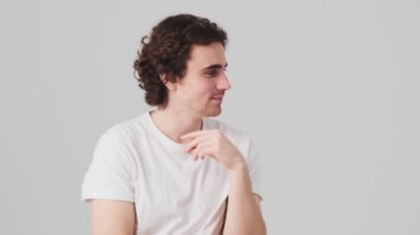 The pensive man holding index finger to cheek making flicking fingers to the sides and smiling at the camera while standing in the studio