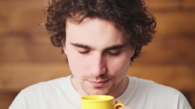 The close-up view of a curly-haired man exhaling aromas from a cup and smiling at the camera