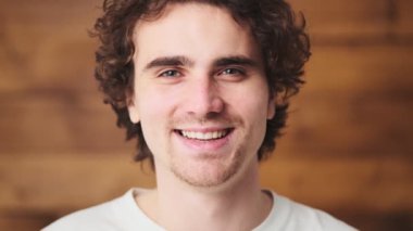The close-up view of the face of a smiling curly-haired man laughing at the camera in the wooden studio