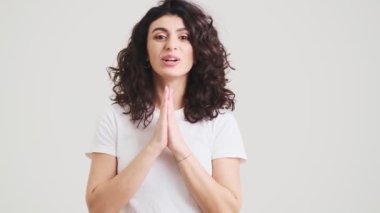 The smiling woman saying please putting her palms to each other while standing in the studio