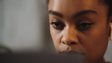 The close-up view of a black woman's face with headphones looking straight into a laptop