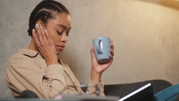 カップを手に持ち音楽を聴きながらヘッドフォンをしている黒人女性の笑顔の側面図 — ストック動画