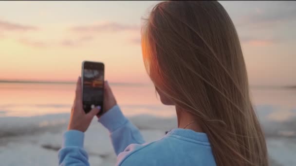 一位金发碧眼的年轻女子正在用她的智能手机拍摄黎明时分在大自然中漫步的照片 — 图库视频影像