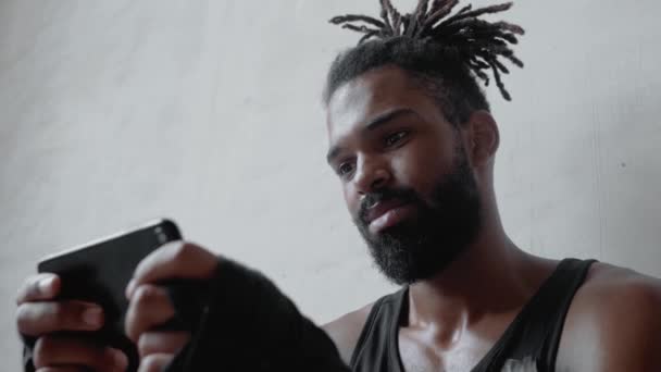 Attractive Young Afro American Sportsman Dreadlocks Using His Smartphone Sitting — Αρχείο Βίντεο