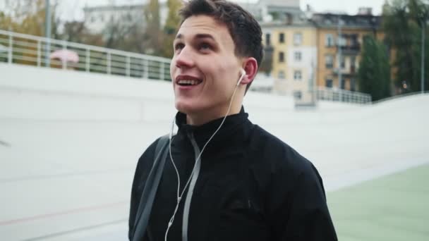 Щасливий Усміхнений Молодий Бігун Слухає Музику Під Час Прогулянки Стадіоні — стокове відео