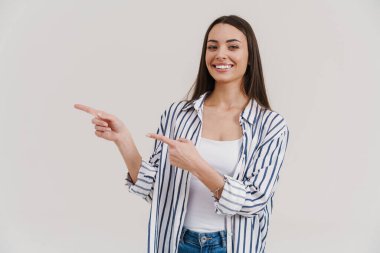 Mutlu güzel esmer kız gülümsüyor ve beyaz arka planda izole edilmiş parmakları işaret ediyor.