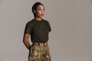 Kendine güvenen Afro-Amerikan askeri kadın. Gri duvarın üzerinde tek başına poz veriyor ve bakıyor.