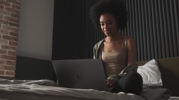 部屋のベッドの上に座っている間 黒の女性は笑って ノートパソコンの画面を見て — ストック動画