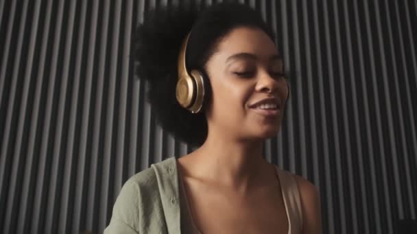 部屋にヘッドフォンで音楽を聴いている笑顔の黒人女性の肖像画 — ストック動画