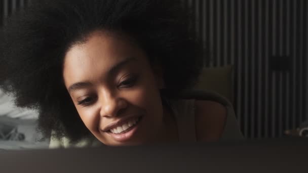 部屋のソファの上に横たわっている間 ノートパソコンの画面を見て笑顔の黒人女性の顔のクローズアップショット — ストック動画