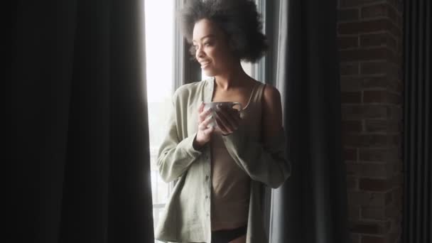 Elinde Bardakla Düşünceli Bir Kadın Odanın Penceresinin Önünde Dikiliyor — Stok video