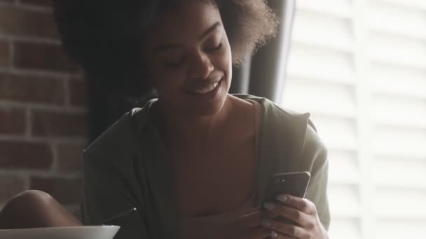 Retrato Una Mujer Negra Sonriente Mirando Teléfono Una Habitación Luminosa — Vídeo de stock