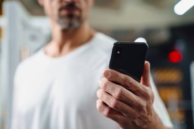 Odaklanmış gri yetişkin sporcu cep telefonu kullanıyor ve spor salonunda çalışıyor.