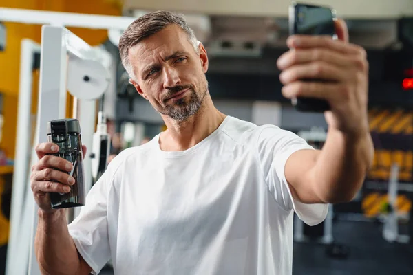 Attraktiver Selbstbewusster Junger Mann Macht Selfie Fitnessstudio Und Zeigt Wasserflasche — Stockfoto