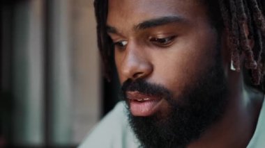 Kulaklıklı, yakışıklı, Afro-Amerikan bir adamın, sokakta otururken dizüstü bilgisayarını kullandığı yakın plan görüntüsü.