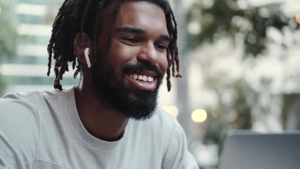 Щасливий Афроамериканський Чоловік Навушниками Використовує Свій Ноутбук Сидячи Вулиці — стокове відео