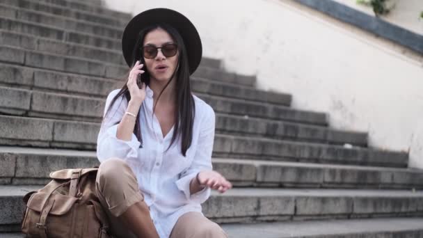 Şapkalı Olumlu Bir Kadın Yazın Merdivenlerde Oturmuş Akıllı Telefonuyla Konuşuyor — Stok video