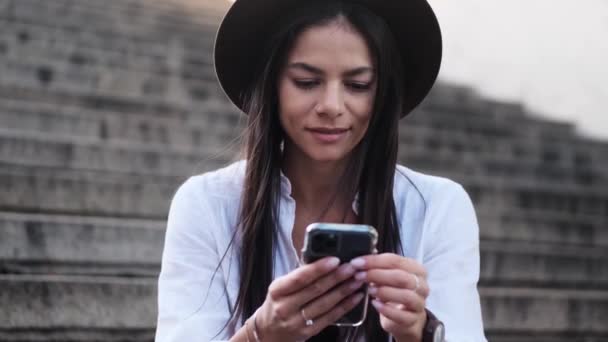 Atrakcyjna Młoda Kobieta Kapeluszu Używa Telefonu Komórkowego Siedząc Latem Schodach — Wideo stockowe