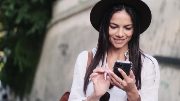 一位面带微笑的年轻女子正在用她的智能手机环顾四周站在外面的街上 — 图库视频影像