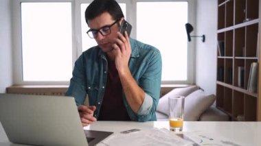 Gözlük takan ciddi bir adam sabahları laptopuyla evde otururken birini arıyor.