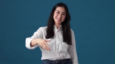 Dost canlısı Koreli bir kadın elini sallarken davet edici bir jest yapıyor. Stüdyonun mavi duvarında tek başına duruyor.