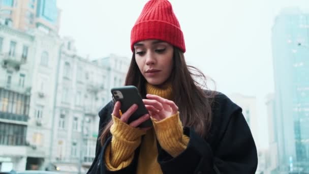 Vrouw Een Jas Hoed Kijkt Naar Telefoon Dan Aan Zijkanten — Stockvideo