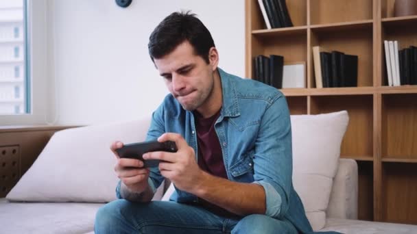 Hombre Concentrado Está Jugando Teléfono Inteligente Mientras Está Sentado Sofá — Vídeo de stock