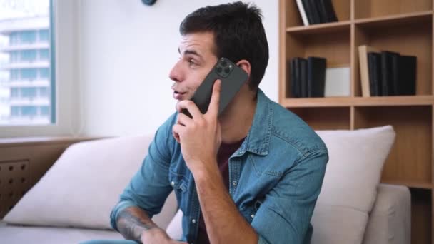 Hombre Guapo Está Hablando Teléfono Inteligente Mientras Está Sentado Sofá — Vídeo de stock