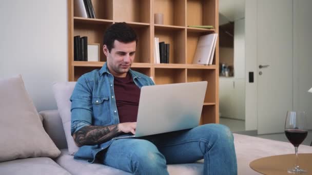 Homem Positivo Está Usando Seu Computador Portátil Enquanto Senta Sofá — Vídeo de Stock