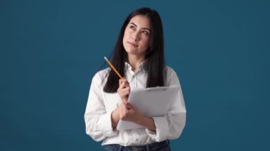 Pozitif Koreli bir kadın elinde kağıt belgeler tutarken stüdyodaki mavi duvarın üzerinde tek başına duran notlar tutuyor.