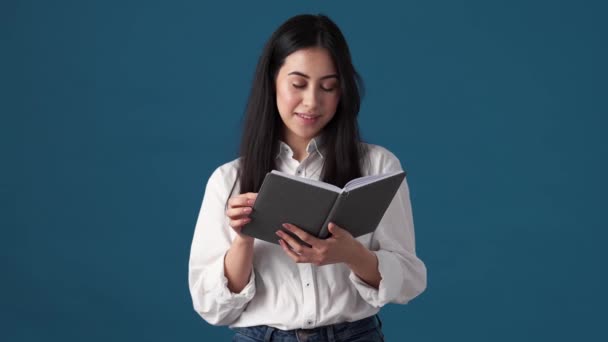 Een Positieve Koreaanse Vrouw Leest Een Boek Geïsoleerd Boven Blauwe — Stockvideo