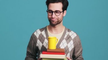 Mavi bir stüdyoda başını sallarken elinde kitap ve bardak tutan yorgun adam.