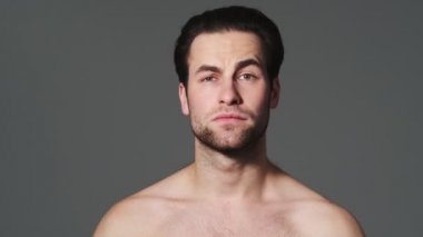 Ciddi bir yarı çıplak adam stüdyodaki gri duvarın üzerinde duran kameraya dur işareti yapıyor.