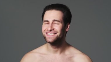 Ciddi bir yarı çıplak adam, stüdyodaki gri duvarın üzerinde ellerini kameraya doğru uzatırken dur işareti yapıyor.