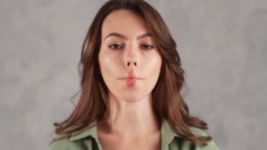 Gri stüdyoda yüzünü buruşturan gülümseyen bir kadının yakın çekimi.