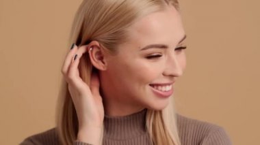 Çekici sarışın bir kadının yakın çekim görüntüsü kameraya poz verirken stüdyodaki bej bir arka planda izole bir şekilde duran bir hava öpücüğü gönderiyor.